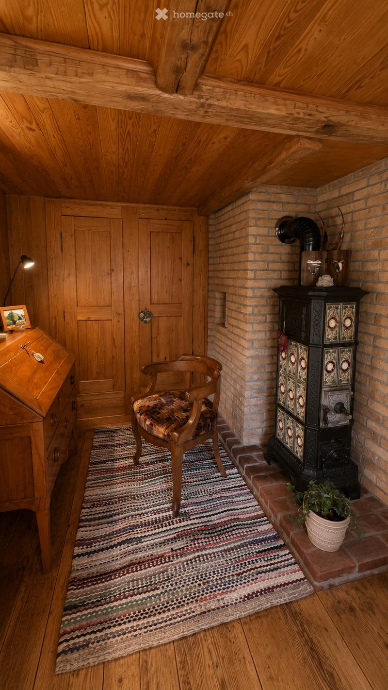 Cozy attic room with wooden walls and ceiling, featuring a wooden stove, a patterned rug, a wooden chair, a wooden dresser, and a small potted plant.