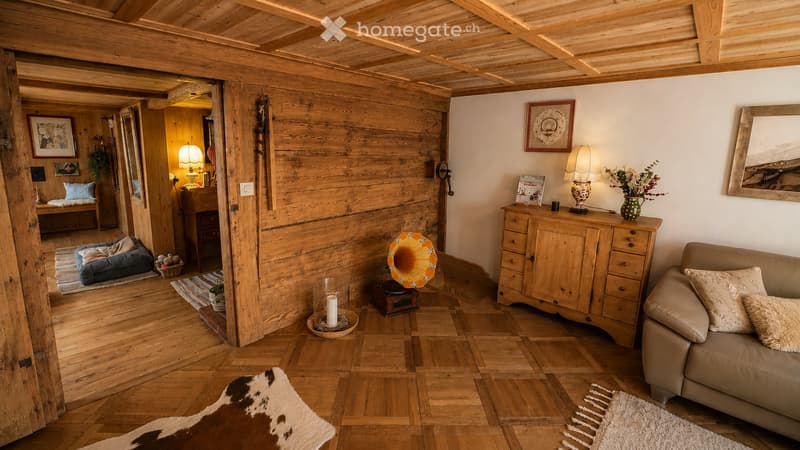 Cozy living room with wooden beams, exposed wooden walls, and a mix of modern and rustic decor including a sofa, table, lamps, and a gramophone.