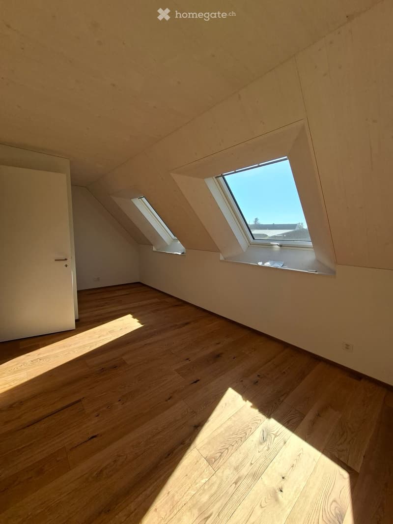 Unfurnished Room. Empty attic room with wooden flooring, slanted wooden ceiling, and two skylight windows allowing natural light to enter.