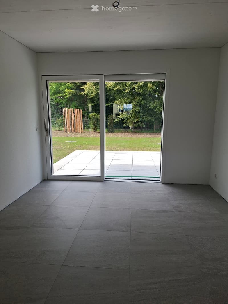 Unfurnished Room. Empty room with large sliding glass doors leading to a patio and garden area. The room has a tiled floor and white walls.