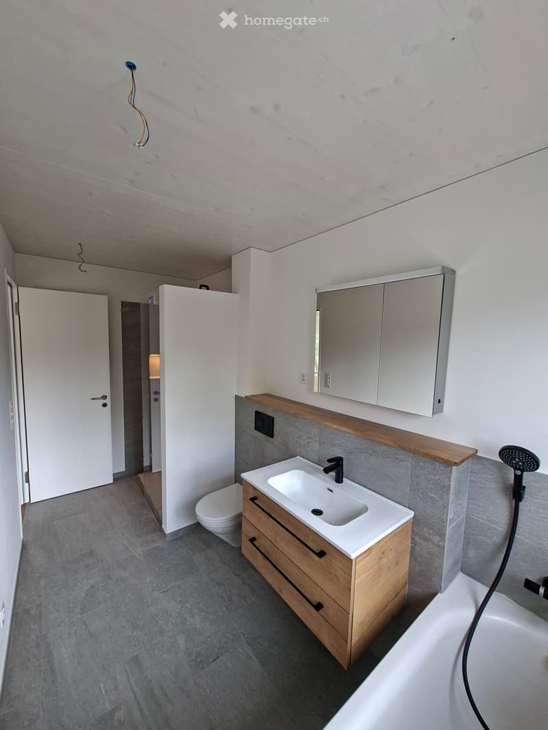 Bathroom. Modern bathroom with a white sink, wooden cabinet, mirror, toilet, and bathtub. Grey tiles on the walls and floor.