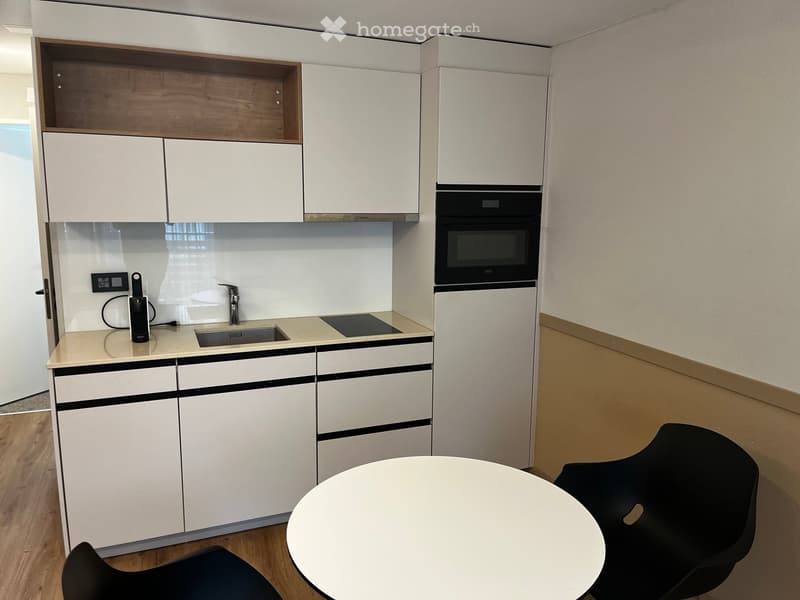Modern kitchen with white cabinets, a sink, an oven, and a small dining area with a round table and two chairs.