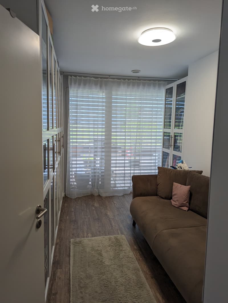 Living room with a brown sofa, a beige rug, and a large window with white blinds.