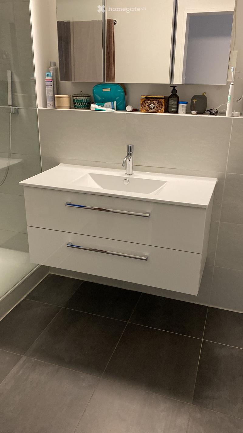 Modern bathroom with a white sink, chrome faucet, mirrored cabinet, and various toiletries on the counter.