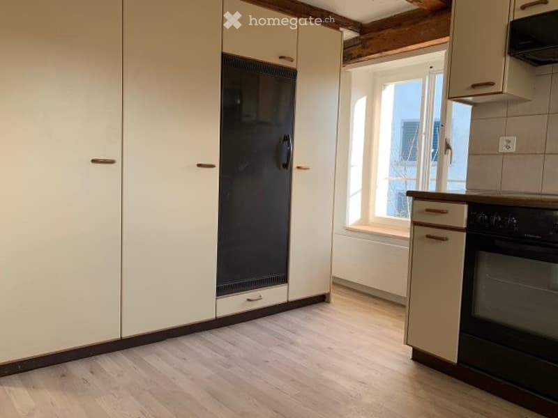 Empty kitchen with light-colored cabinets, a black refrigerator, and a window with a view of the city.