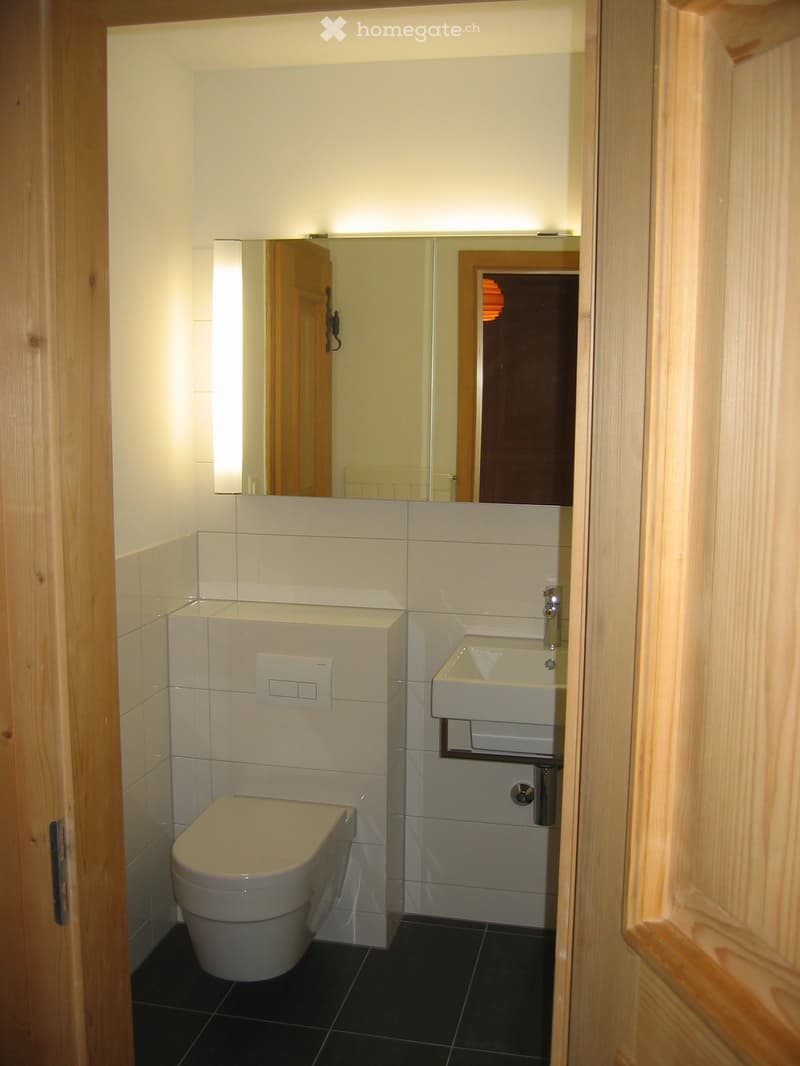 Modern bathroom with white tiles, black floor, toilet, sink, and mirror.