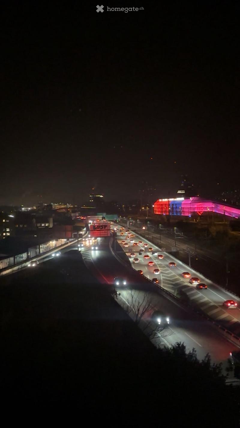 Nighttime aerial view of a busy highway with multiple lanes of traffic, illuminated vehicles, and distant city lights.