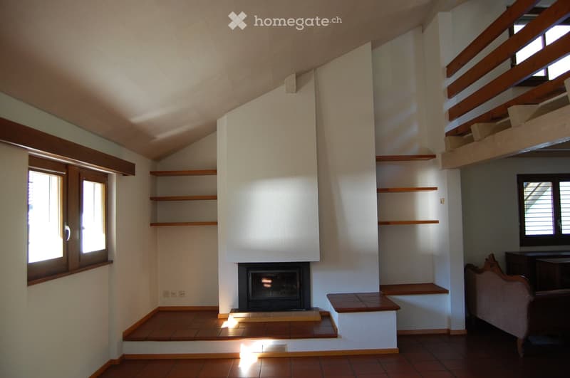 Living room with a fireplace, wooden shelves, and a staircase leading to an upper level.