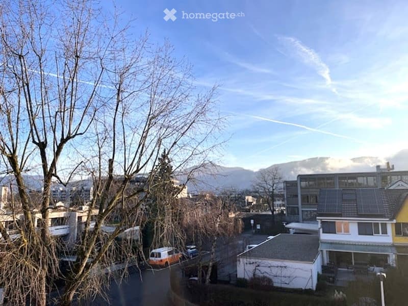 View of a residential area with buildings, trees, and mountains in the background under a clear blue sky.