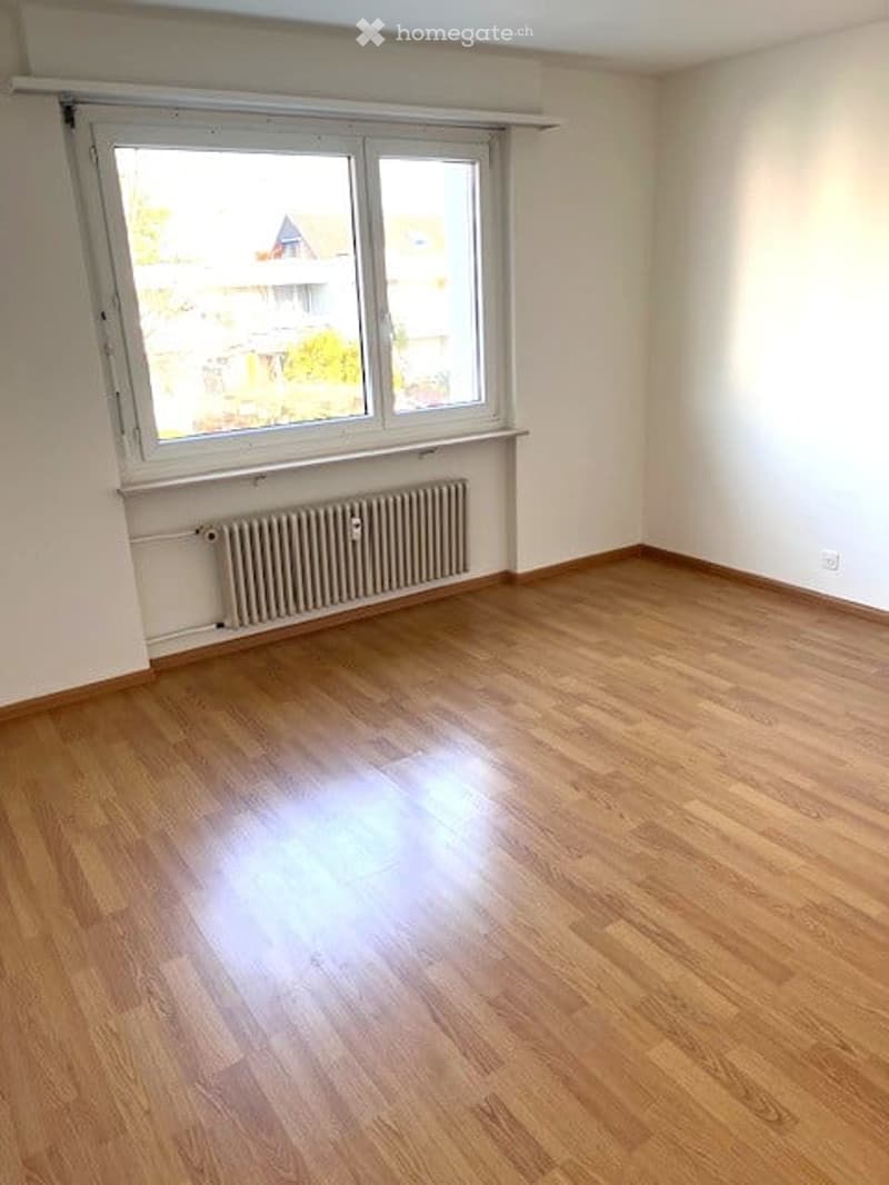 Empty room with wooden flooring, white walls, and a large window with a radiator below it.
