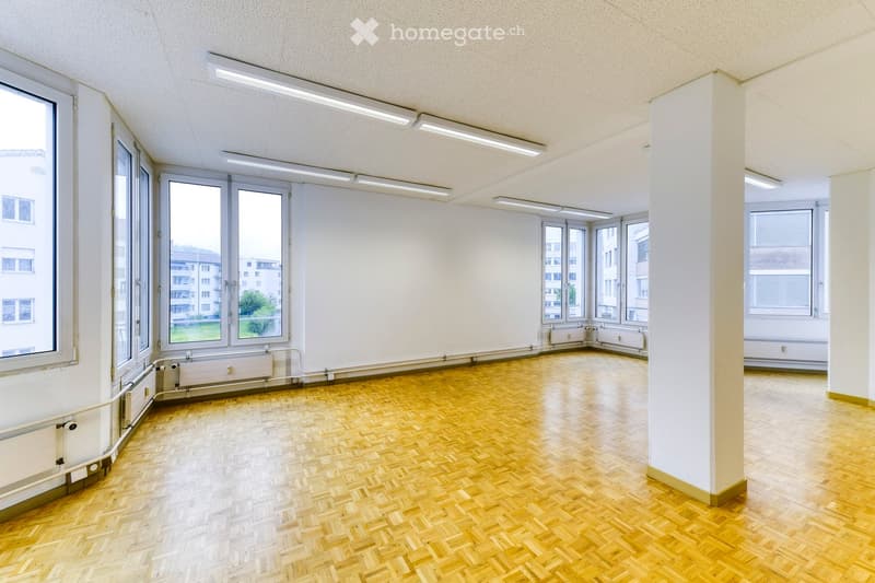 Empty room with wooden herringbone flooring, white walls, large windows, and recessed lighting. No furniture or equipment present.