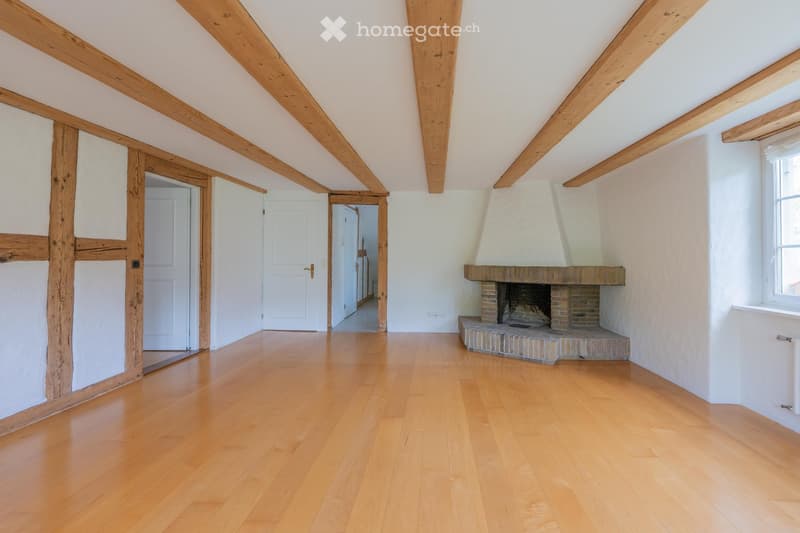 Empty room with wooden beams, polished wooden floor, fireplace, and white walls.