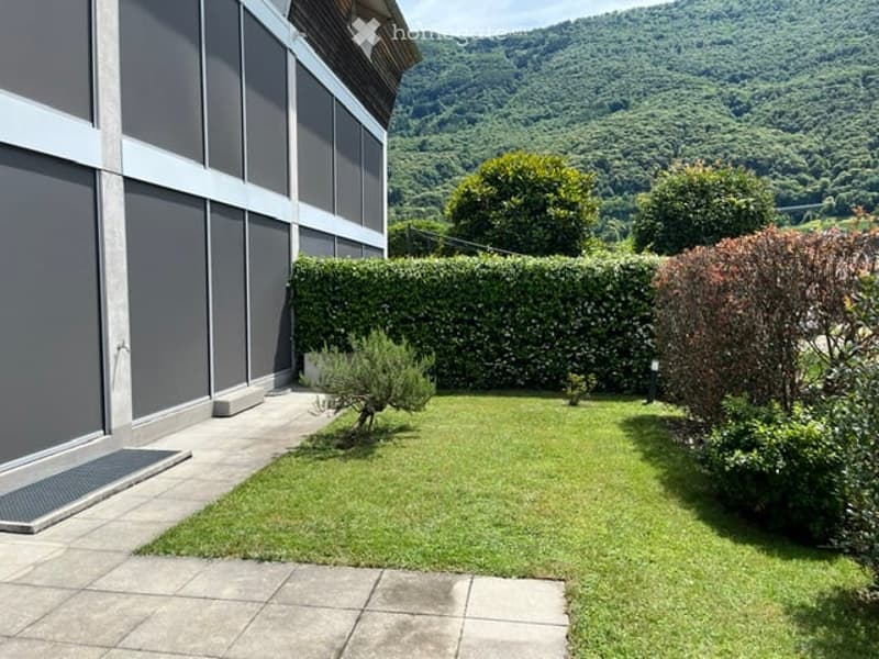 Well-maintained garden with neatly trimmed hedges, small trees, and a view of green hills in the background.