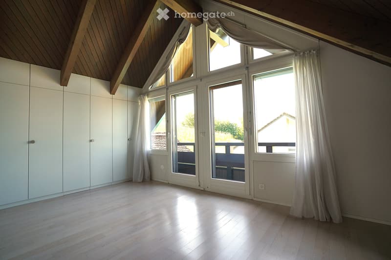 Bright, empty room with wooden flooring, white built-in wardrobes, large windows with white curtains, and a sliding glass door leading to a balcony.