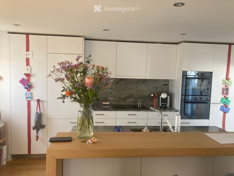 Modern kitchen with white cabinets, wooden counter, vase with flowers, and various appliances.
