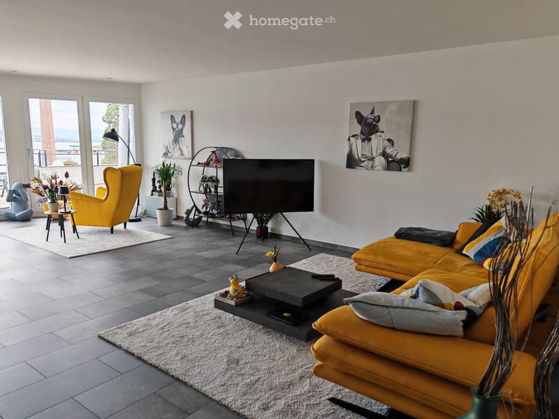 Modern living room with a yellow sofa, armchair, coffee table, TV, and decorative items. Large windows offer a view of the balcony.
