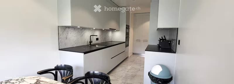 Modern kitchen with white cabinets, black countertops, a sink, and a small dining area with chairs and a table.
