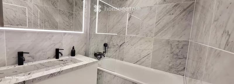 Modern bathroom with marble tiles, double sink, bathtub, and large mirror.