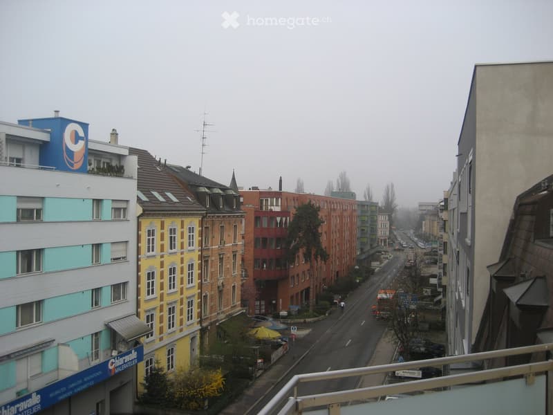 A street view showing a mix of residential and commercial buildings with colorful facades, parked cars, and a few pedestrians.