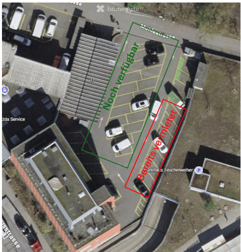 Aerial view of a building with a parking lot, marked areas for parking, and surrounding structures.