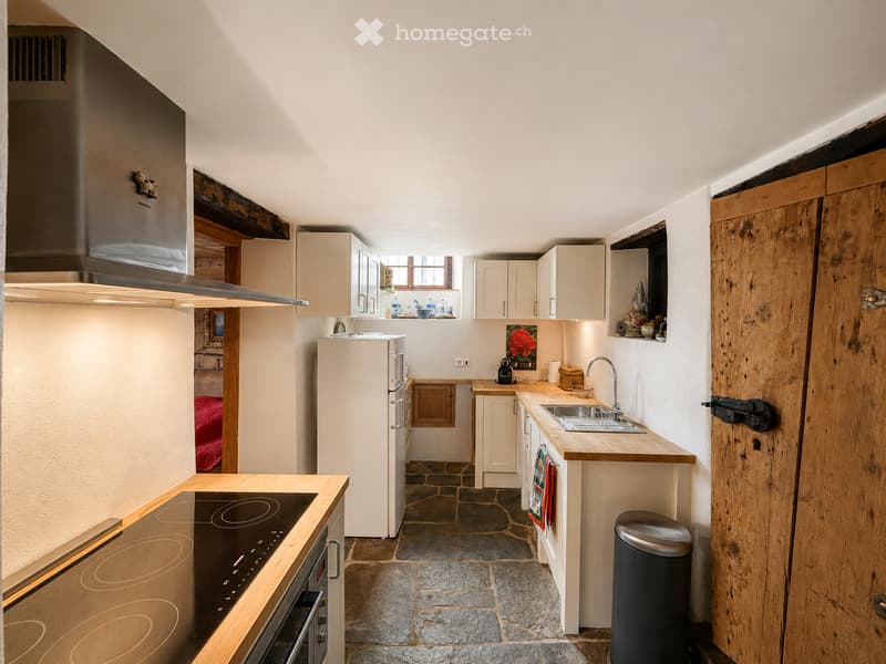 Modern kitchen with white cabinets, stainless steel appliances, wooden countertops, and a stone floor.