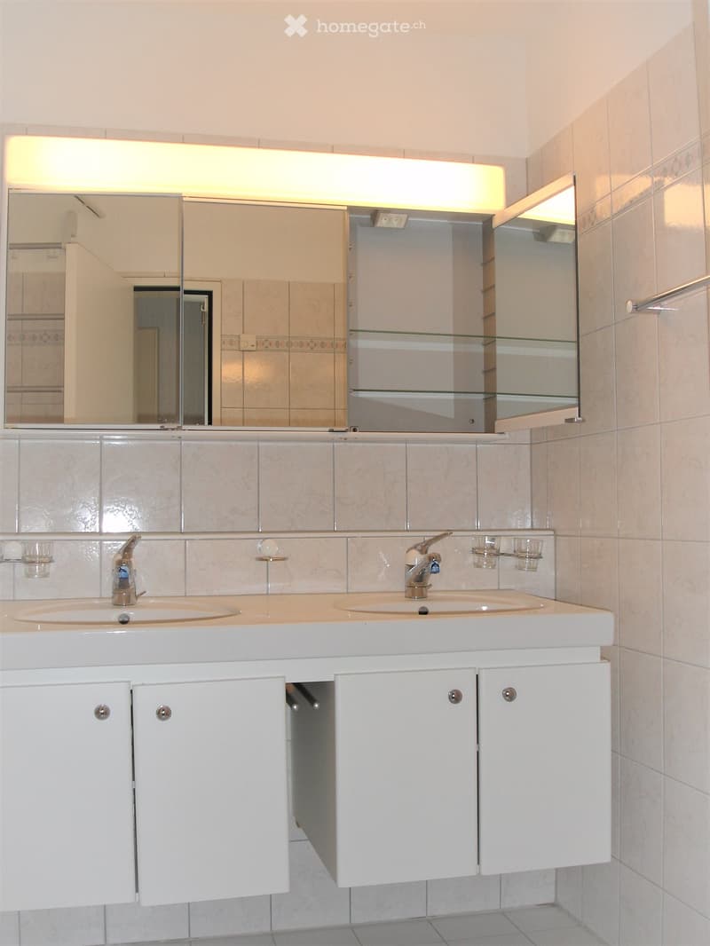 modern bathroom with double sink, mirror, cabinets, and tiled walls