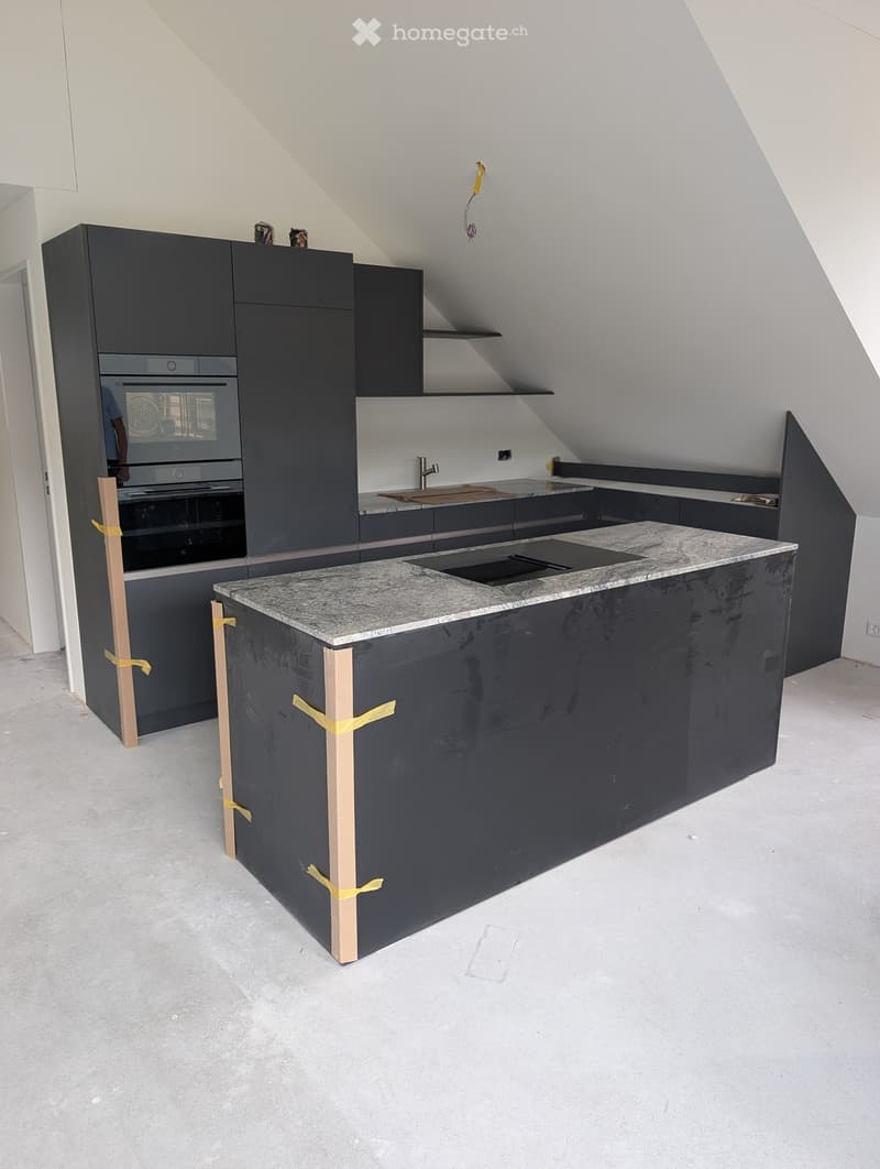 Modern kitchen with dark grey cabinets, marble countertop, built-in oven, sink, and faucet. The island is partially covered with protective tape.
