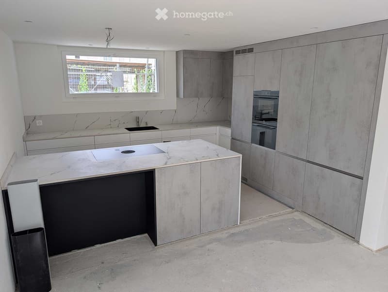 Modern kitchen with marble countertops, grey cabinets, and built-in appliances including a sink and oven. Features a large island with a central countertop.