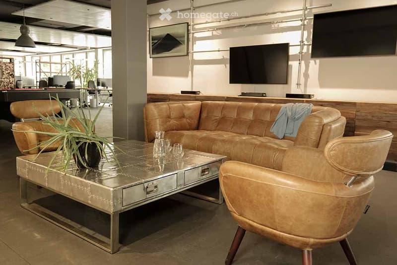 Modern living room with a leather sofa, a metal coffee table, a leather armchair, a plant, and a television mounted on the wall.