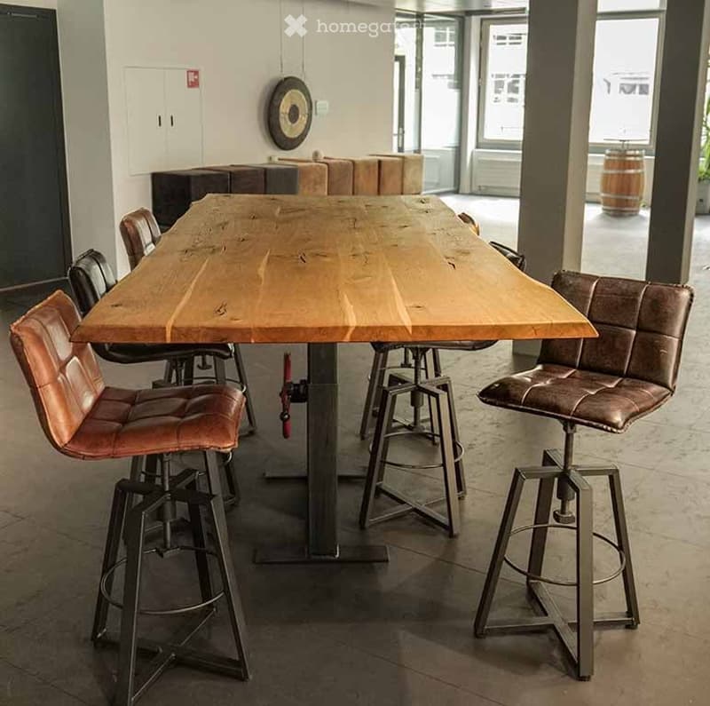 A modern, industrial-style room with a large wooden table and several leather stools, featuring exposed metal legs and a minimalist design.