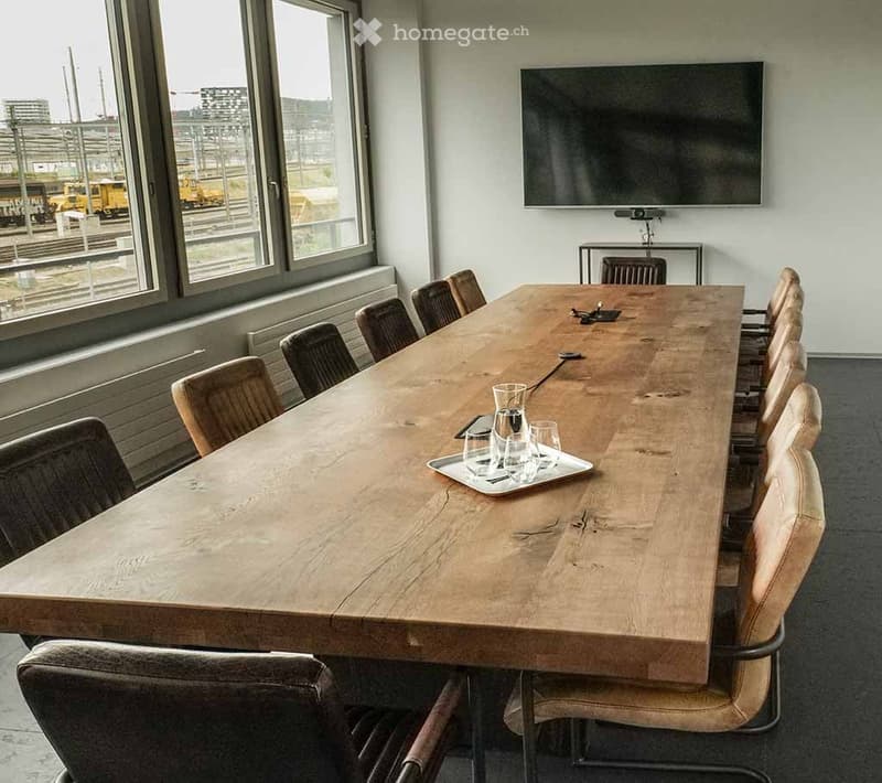 A modern conference room with a long wooden table, multiple chairs, a large flat-screen TV, and a tray with glasses and a pitcher.