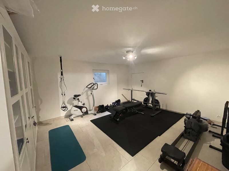 A well-lit room with exercise equipment including a bike, bench, and weight machine, along with a blue exercise mat and a black workout mat.