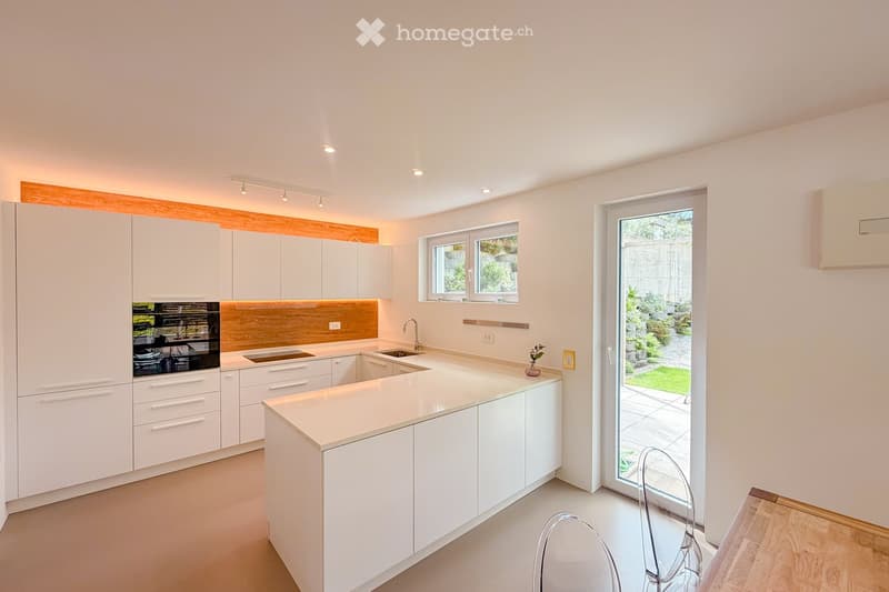 Modern kitchen with white cabinets, a central island, and a wooden backsplash. Features include a sink, faucet, and an oven, with a sliding glass door leading to an outdoor area.