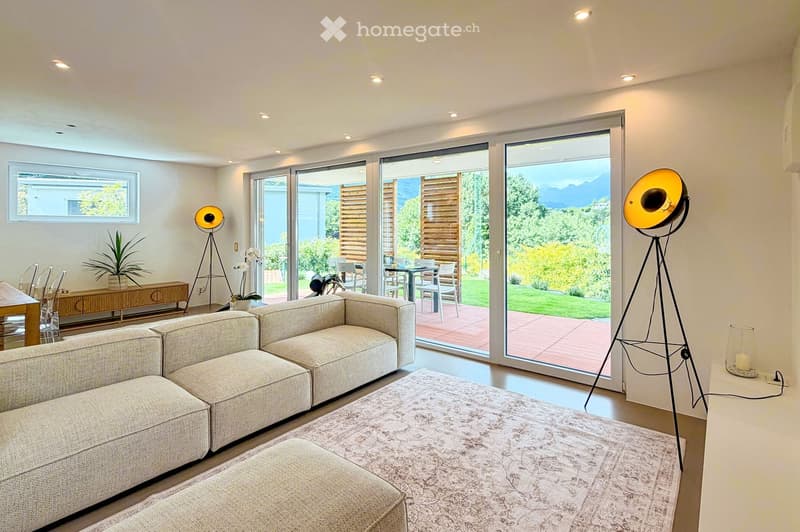 Modern living room with large sliding glass doors leading to a patio, a sectional sofa, coffee table, floor lamps, and a dining area with a table and chairs.