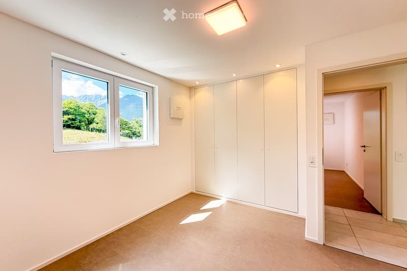 Empty room with white walls, tiled floor, large windows showing a scenic mountain view, and built-in white closet units.