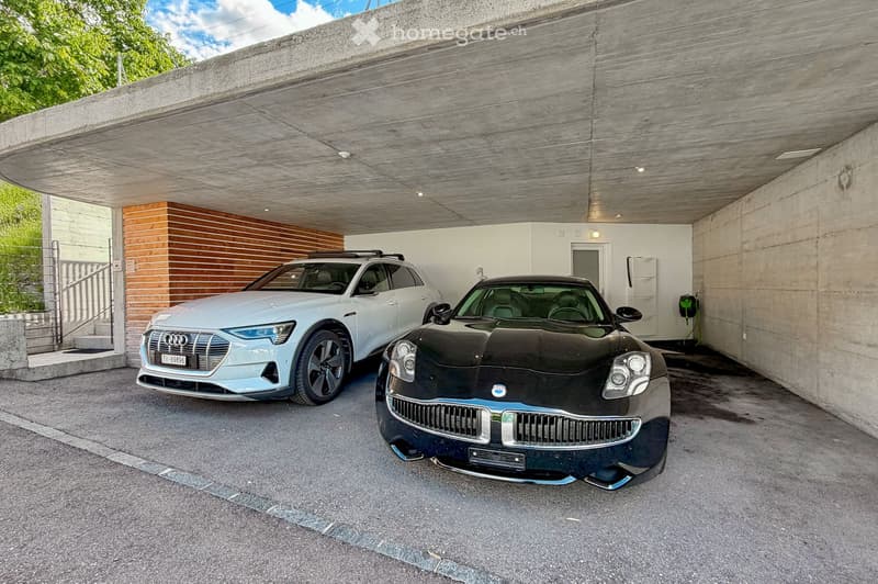 {"type": "Garage", "objects": [], "visible_features": ["Garage"], "description": "Modern underground garage with two parked cars, a light grey SUV and a black sports car, concrete walls and ceiling, and a staircase leading upwards.", "localized_descriptio