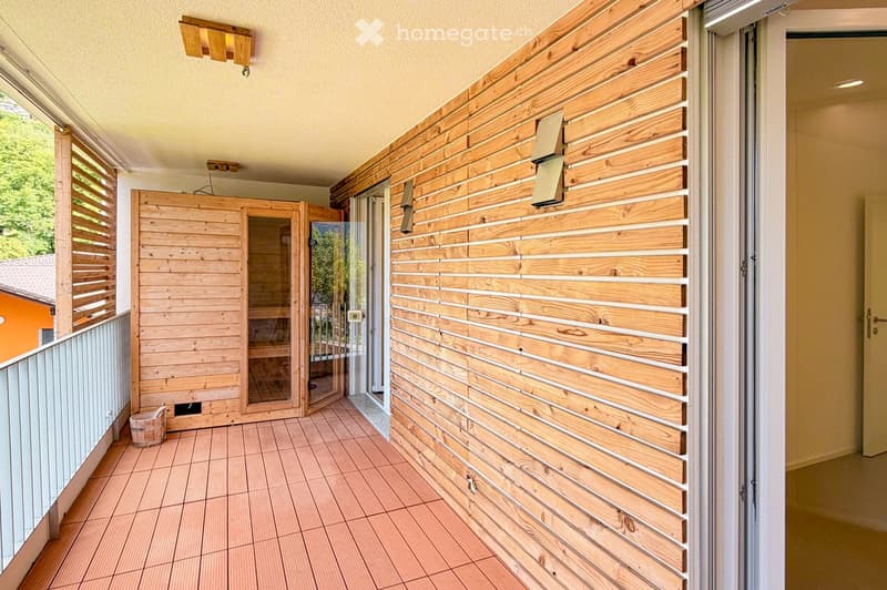 Balcony with wooden slatted walls, tiled floor, and a small wooden sauna enclosure with glass doors.