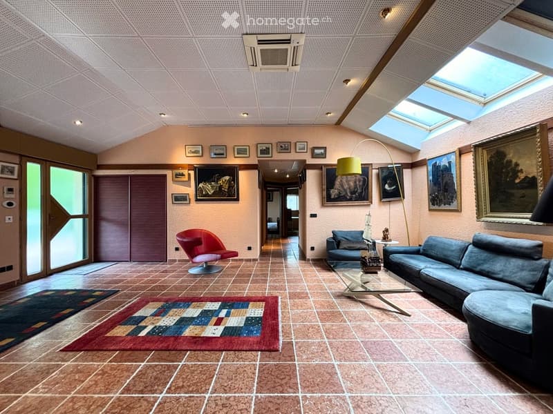 Living room with a blue sectional sofa, red swivel chair, glass coffee table, floor lamp, and several picture frames on the walls.