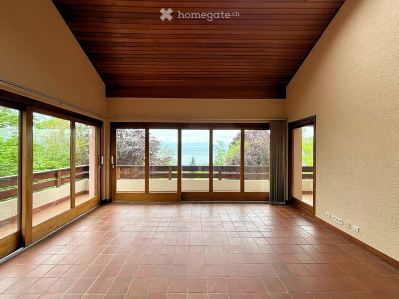 Empty room with wooden ceiling, terracotta tiled floor, large sliding glass doors leading to a balcony with wooden railing and scenic view.
