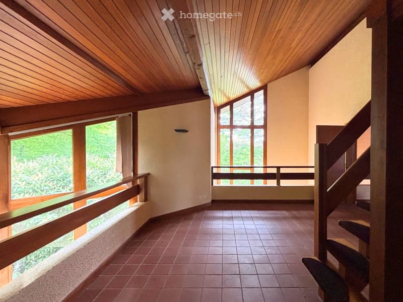 Open, airy hallway with wooden ceiling, large windows, and a staircase leading upwards.
