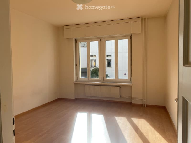 Empty room with wooden flooring, large windows, built-in cabinets, and a radiator below the windows.