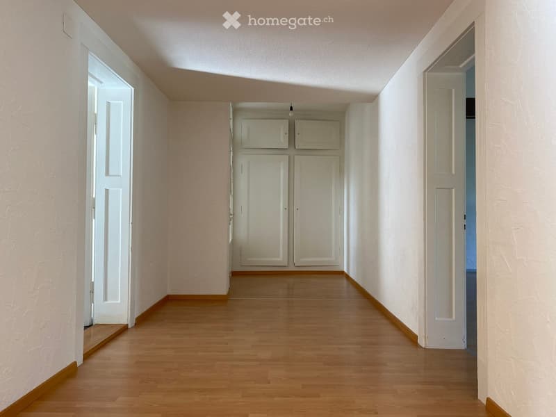 Empty hallway with wooden flooring, white walls, and several closed doors leading to other rooms.