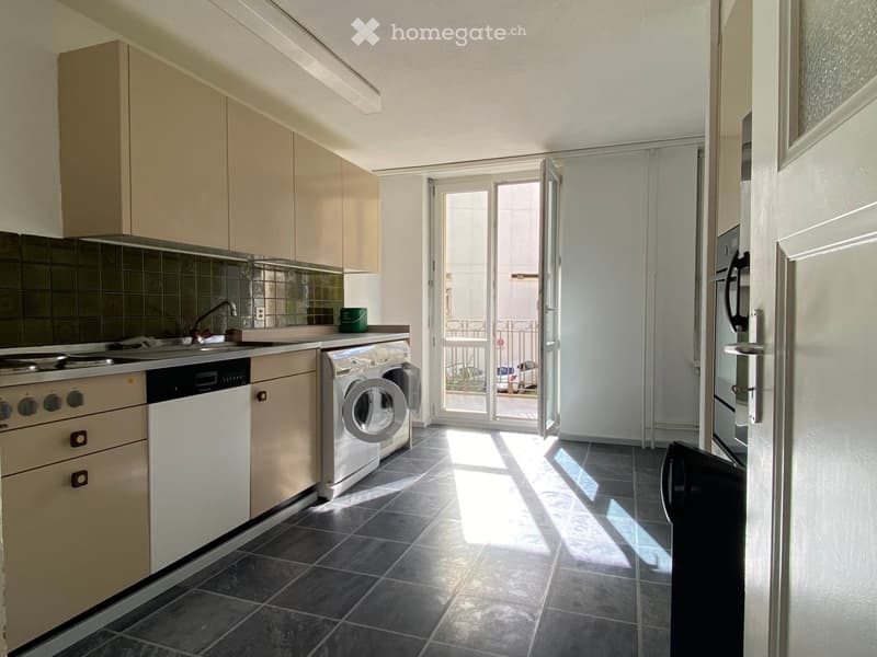 Modern kitchen with light-colored cabinets, dark tiled floor, and a sliding glass door leading to a balcony. Appliances include a refrigerator, oven, dishwasher, and washing machine.