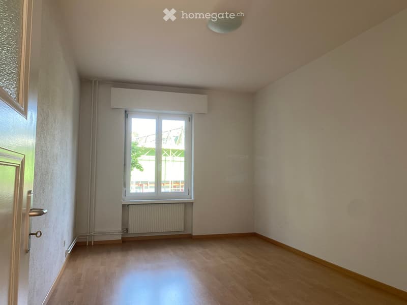 Empty room with wooden flooring, light-colored walls, a window with white frame, and a radiator below it.