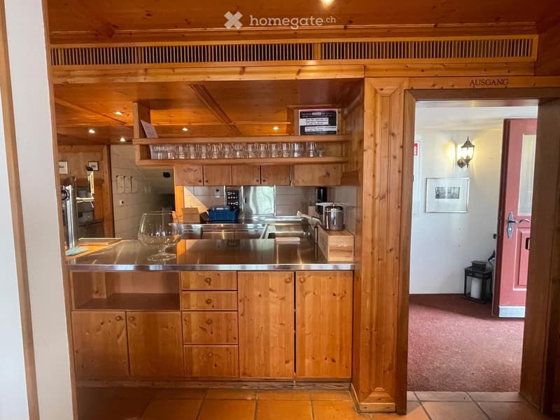 A rustic kitchen with wooden cabinets, a stainless steel sink, and a countertop with glassware and a pot. The space features exposed wooden beams and a warm, inviting atmosphere.