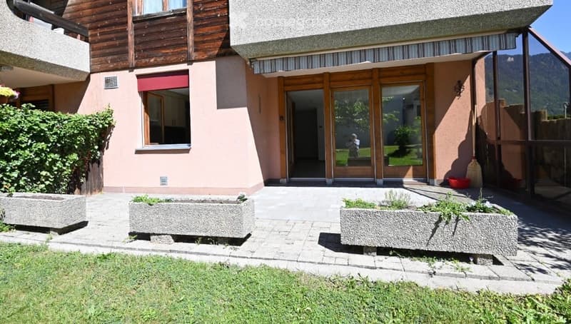 Two-story residential building with a modern facade, large glass doors, and a well-maintained garden area with stone planters and a paved walkway.