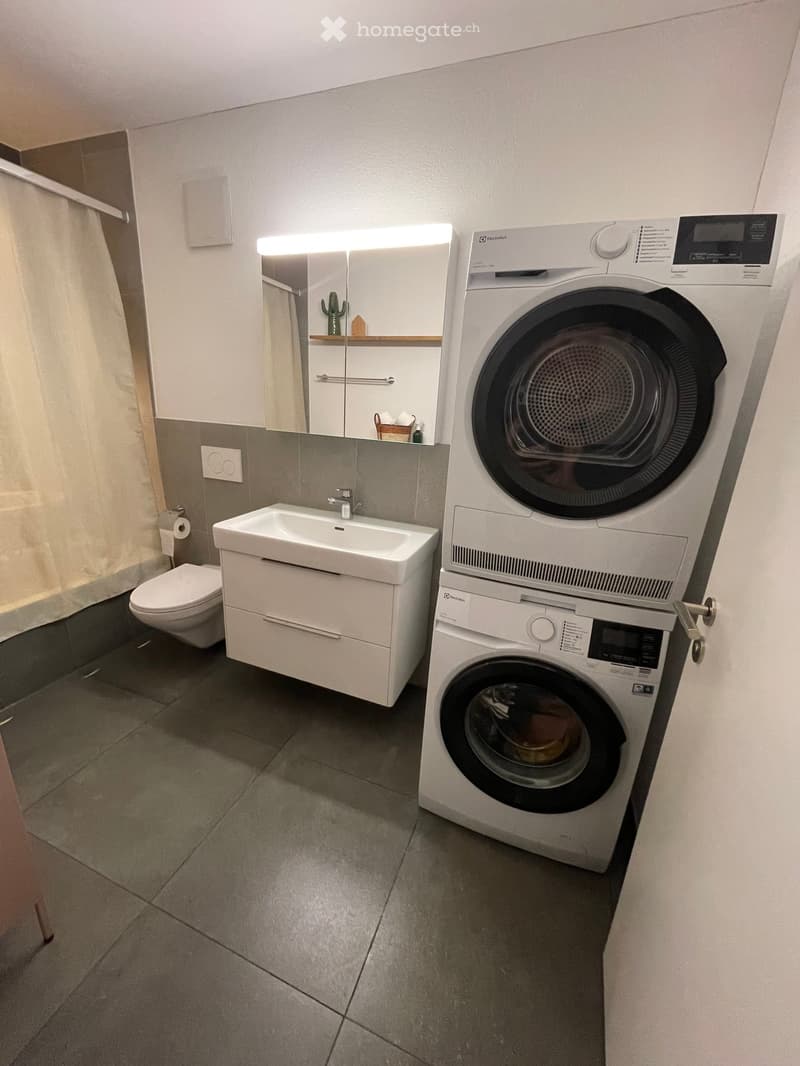 Modern bathroom with a sink, toilet, mirror, and stacked washing machine and dryer unit.