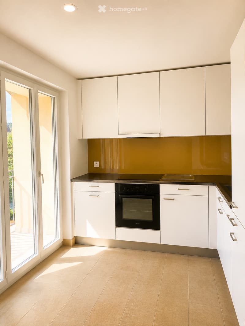 Modern kitchen with white cabinets, a black oven, and a warm-toned backsplash. Large windows allow natural light to fill the space.