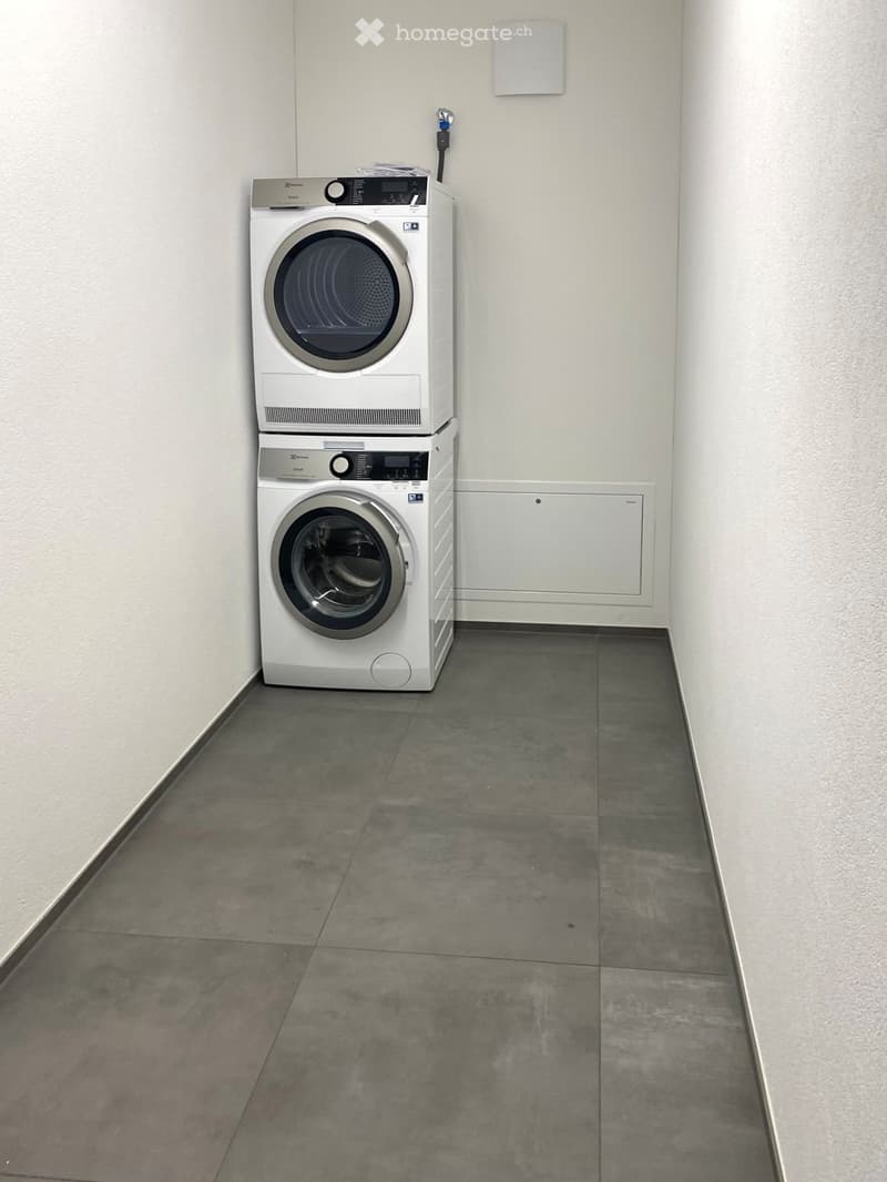 Empty room with concrete floor and white walls, featuring a stacked washer and dryer unit.