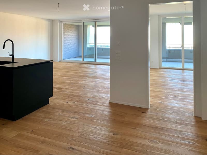 Empty room with wooden flooring, a black kitchen island with a sink, and large glass sliding doors leading to a balcony.